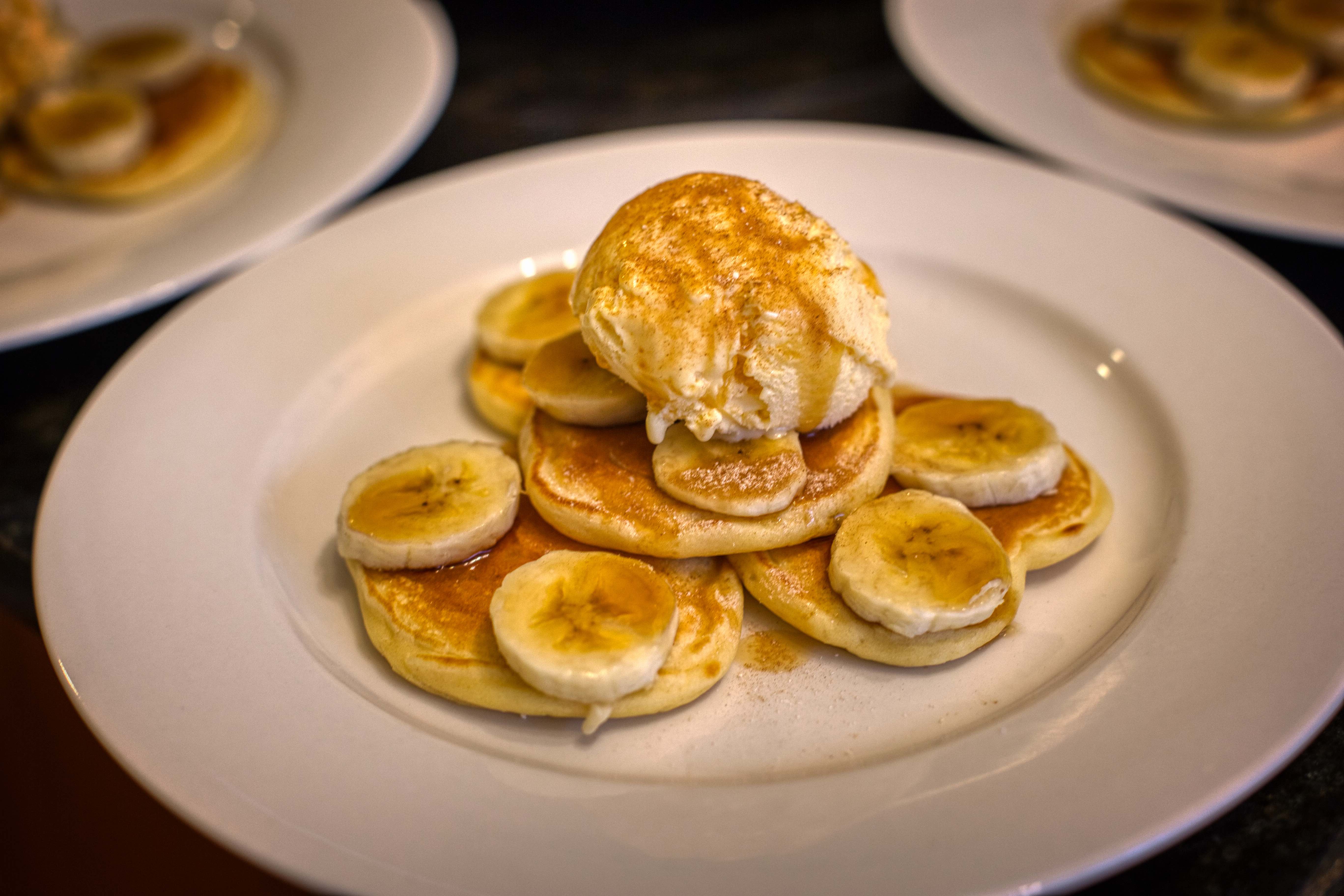 Pancakes with sliced banana, a blob of vanilla ice-cream, maple syrup and sprinkled with cinnamon